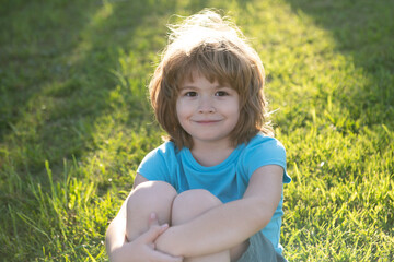 Fototapeta premium Happy child, adorable lovely kid on grass. Joyful portrait of small child on green nature background outside.