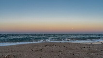 Evening on the Red Sea coast. The full moon shines in the blue-pink sky. Turquoise waves roll onto the sandy beach and foam. Egypt