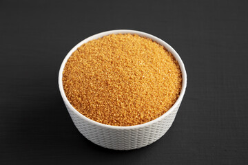 Brown Demerara Sugar in a Bowl on a black background, side view.