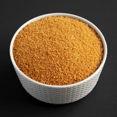 Brown Demerara Sugar in a Bowl on a black background, low angle view.