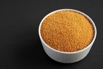 Brown Demerara Sugar in a Bowl on a black background, side view. Copy space.