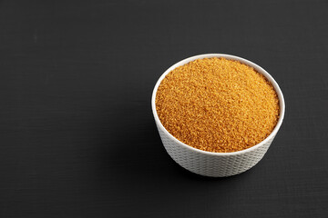 Brown Demerara Sugar in a Bowl on a black surface, low angle view. Copy space.
