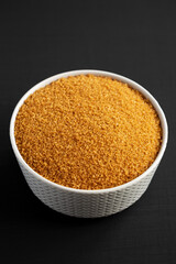 Brown Demerara Sugar in a Bowl on a black surface, side view.