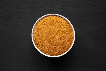 Brown Demerara Sugar in a Bowl on a black surface, top view. Flat lay, overhead, from above.