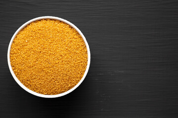 Brown Demerara Sugar in a Bowl on a black surface, top view. Flat lay, overhead, from above. Space for text.