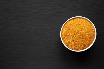 Brown Demerara Sugar in a Bowl on a black     background, top view. Flat lay, overhead, from above. Copy space.