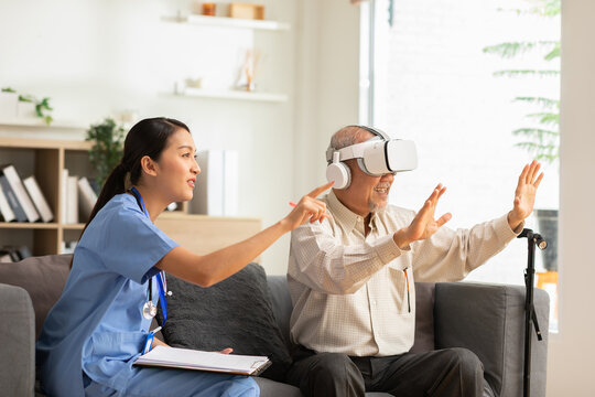 Asian Female doctor give advice elderly patient using VR or Virtual Reality glasses headset pointing objects or touching tracking health.Happy senior man having fun with goggle using VR enjoy at home