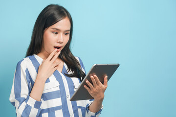 Fototapeta premium Asian teen looking at smartphone and feeling wow with shock deal in app isolated on blue background.