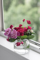 Bouquet with pink and white peonies and garden roses in a vase on the windowsill against the background of an open window.