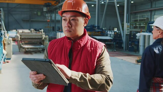 Young asian man heavy industrial worker with helmet using a digital tablet in factory. Look around. Checking product progress.