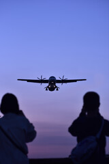 Naklejka na ściany i meble A plane landing to airport runway at sunsett, two silhouettes of people