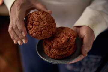An anonymous woman is holding several cookies and a gray ceramic plate in her hands