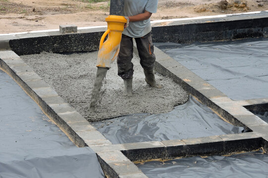 A building worker pouring a concrete slab foundation using a hose of a concrete pump truck