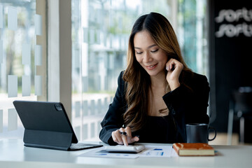 Fototapeta premium A beautiful Asian businesswoman sitting in her private office, she is checking company financial documents, she is a female executive of a startup company. Concept of financial management.