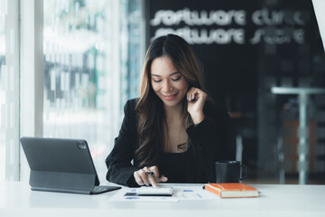 A beautiful Asian businesswoman sitting in her private office, she is checking company financial documents, she is a female executive of a startup company. Concept of financial management.