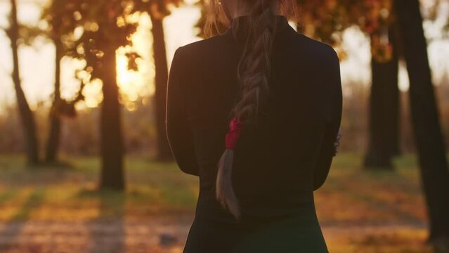 A young woman with Santa Muerte make-up dressed in a black dress of death walks against the backdrop of autumn leaves in the forest during sunset. Day of the Dead or Halloween concept.