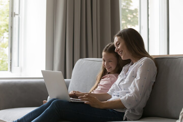 Cheerful happy mom and little kid enjoying family leisure at laptop, watching movie, sitcom,...