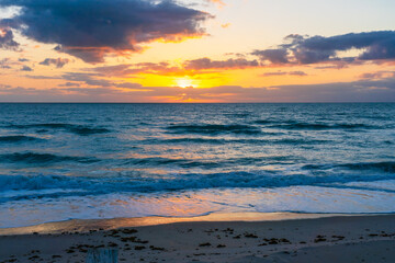 Fototapeta premium Sunrise over the Atlantic Ocean in the early morning in Florida. The sun illuminates the sky with a golden color in the clouds and is reflected on the dark waters of the ocean.