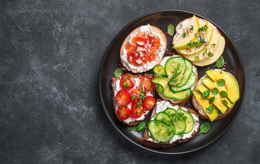Assorted sandwiches with soft cheese, vegetables and fruits on a dark background. Top view, copy space.