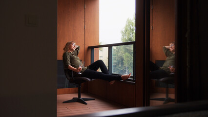 Full shot of a middle-aged caucasian woman sitting on a chair on her balcony with a glass of wine and looking at the sky. High quality photo