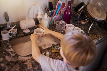 Chores are a vital life skills for kids to learn. High angle shot of a little boy washing dishes in...