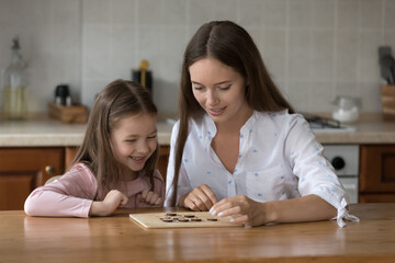 Happy mom and little daughter girl engaged in learning board game. Mother teaching kid to play checker draughts, training tactical and logical skills. Parenthood family leisure time concept