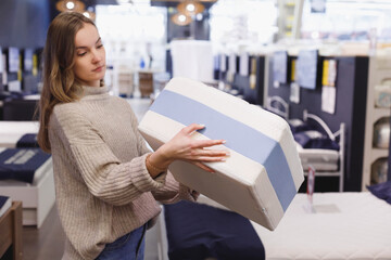 Young woman chooses mattress and bed in furniture showroom store. Sample of mattress in hands, beds...