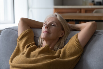 Peaceful sleepy middle aged woman resting on sofa with closed eyes, falling asleep, enjoying break, silent leisure time at home, taking deep breath of fresh air, reducing stress - obrazy, fototapety, plakaty