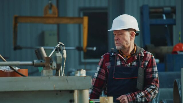 Elder engineer man in safety uniform and hard hat hold tablet computer walking checks production processes in factory. Inspector in warehouse.