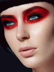 Beautiful brunette girl with red eye shadow and black bob hairstyle and nail. Closeup portrait of a model with bright makeup on a face.