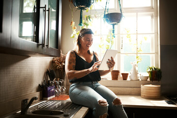 Theres a lot to make you laugh online. Shot of a young woman using a digital tablet in the kitchen at home.