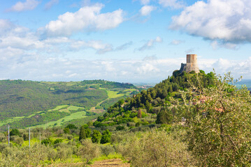 Fototapeta na wymiar Rocca d'Orcia, a medieval village and fortress in Tuscany, Italy. Unique view of the stone tower perched on rock cliff against blue sky with scenic clouds.