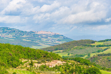 Fototapeta na wymiar Green landscape in Tuscany, Italy. Unique view of medieval village and stone tower perched on rock cliff against dramatic sky.