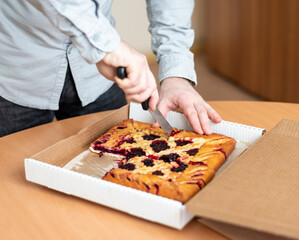 a man cuts a pie with berries in the office, delivering a pie to work. Celebration of an important event by the team.