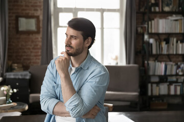 Pensive millennial entrepreneur touching chin in deep thoughts, looking at window away, planning tasks, future career, project vision, thinking over startup. Head shot portrait