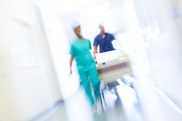 Motion blur ethnic nursing staff in scrubs with hospital bed healthcare centre