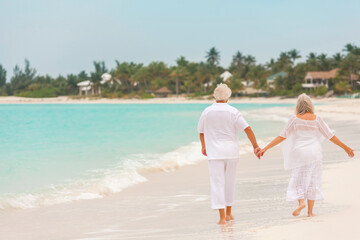 Barefoot Caucasian senior couple in white clothes on a travel resort beach
