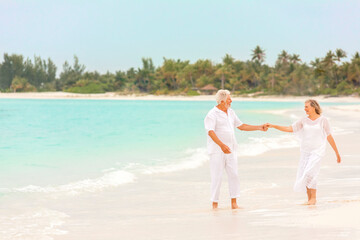 Senior Caucasian couple in white clothes dancing on a tropical beach vacation