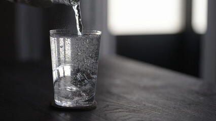 pour tonic water over ice ball in tumbler glass on wood table