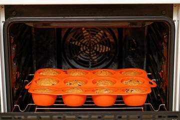 Homemade cherry cupcakes baked in a red silicone mold inside a home oven. Shallow focus.