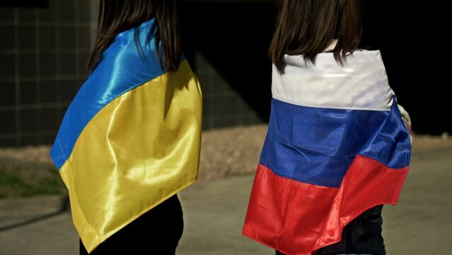 Women with flags of Russia and Ukraine on their shoulders turned away from each other. Rupture of relations between Russia and Ukraine. Hostility, conflict, war, aggression.