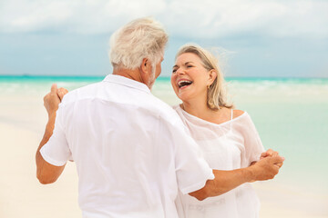 Senior Caucasian couple in white clothes dancing together on a tropical beach
