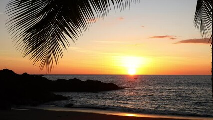 sunset on a tropical beach, swaying palm leaves, holiday atmosphere, natural colors, calm sea glistening in the rays of the setting sun 