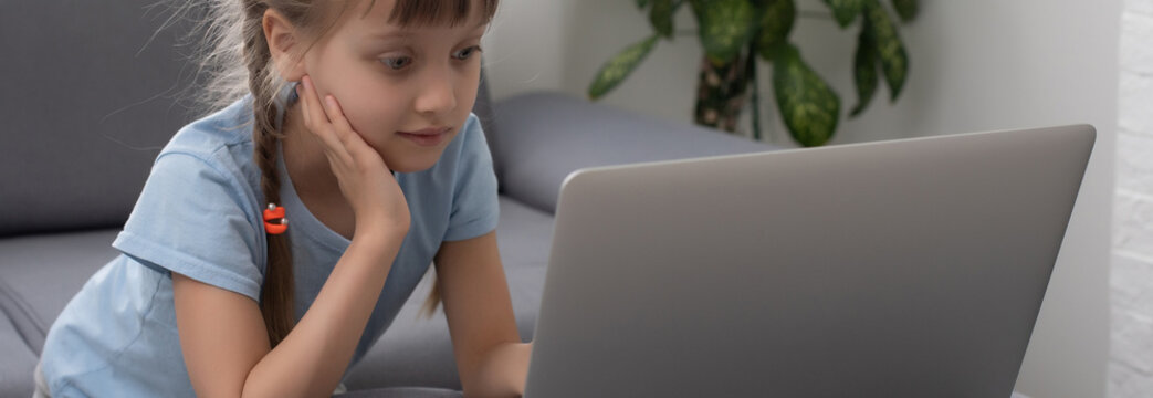 Bored Little Girl With Laptop At Home. Cute Child Doing Homework On Computer. Modern Online Education, Communication And Technology Concept, Copy Space.