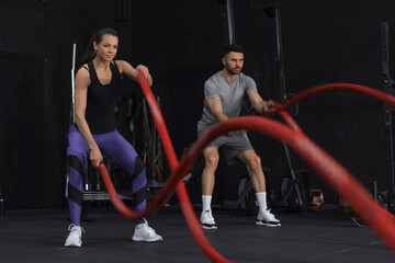 Obraz na płótnie Canvas Athletic young couple with battle rope doing exercise in functional training fitness gym.