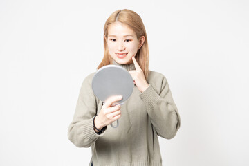 白い背景の前に立って鏡で顔を見る若い女性