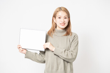 白い背景の前に立って小さいスケッチブックを見せている若い女性