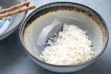 Close-up of a grey bowl with steamed white rice on a concrete background, studio shot