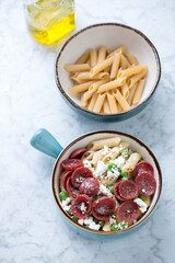 Crispy salami, crushed green pea and ricotta pasta, vertical shot on a light-grey marble background, elevated view