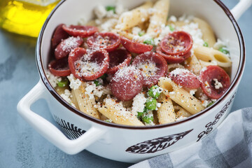 Penne pasta with crispy salami, ricotta cheese and green peas in a serving pan, close-up, selective focus